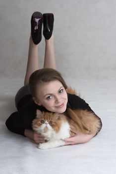 Very nice blonde lies on a floor and holds a red persian kitten