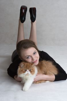 Very nice blonde lies on a floor and holds a red persian kitten