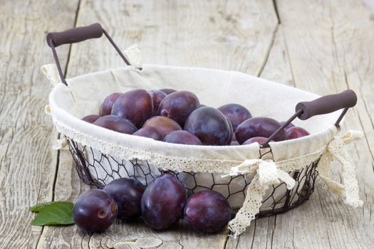 fresh plums in a basket on wooden background