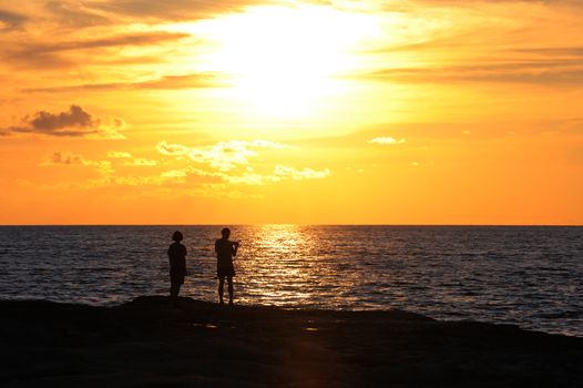 Young couple standing on the shore and looks at the setting sun by the sea
