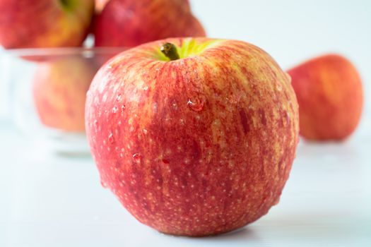 One red apple against others in a glass bowl with white background.