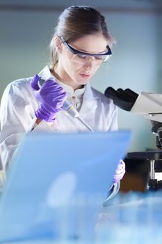 Life scientist researching in laboratory. Portrait of attractive, young, confident female health care professional pipetting under microscope in hes working environment. Healthcare and biotechnology.