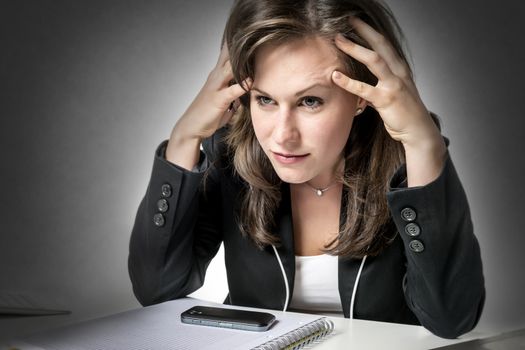 Stressed business woman sitting in office at desk, looking at laptop and holding his hands to his head