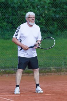 Senior man playing tennis on a gravel court