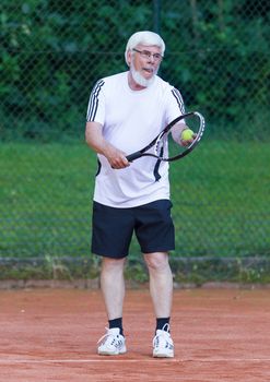 Senior man playing tennis on a gravel court