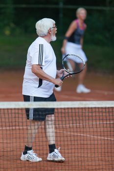 Senior man playing tennis on a gravel court