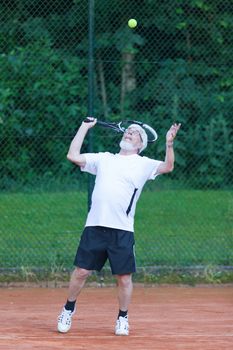 Senior man playing tennis on a gravel court