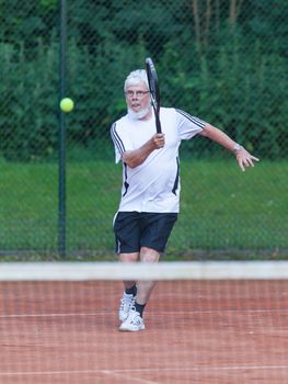 Senior man playing tennis on a gravel court