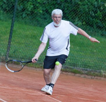 Senior man playing tennis on a gravel court