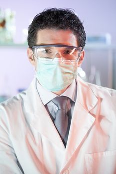 Portrait of a confident male health care professional in his working environment wearing lab coat and protection mask and goggles. Healthcare and biotechnology concept.