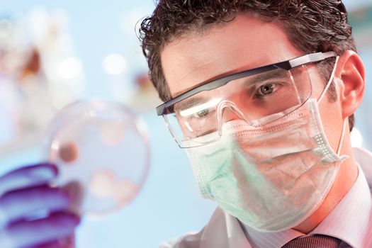 Mask and goggles protected life science researcher observing potentially infectious cells in petri dish. Focus on scientist's eye. Healthcare and biotechnology concept.