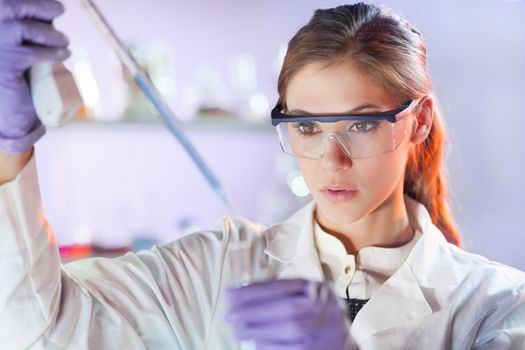 Life scientists researching in laboratory. Focused female life science professional pipetting solution into the glass cuvette. Lens focus on researcher's eyes. Healthcare and biotechnology concept.