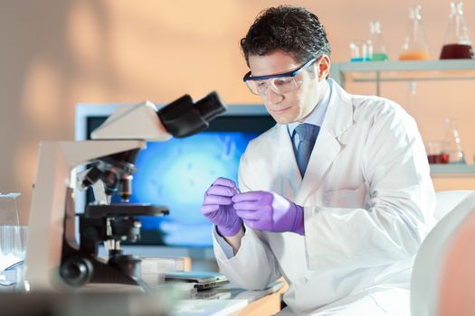 Life scientist researching in laboratory. Attractive young male scientist looking at the microscope slides in laboratory. Healthcare and biotechnology concept.