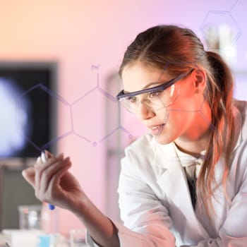 Life science researcher working in laboratory. Portrait of a confident female health care professional in his working environment writing structural chemical formula on a glass board. 