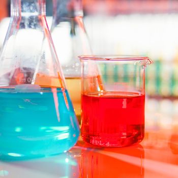 Backlit laboratory test flask containing colorful liquids. Square composition.