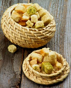 Wicker Bowls with Homemade Dried Herbs Bread Cubes closeup on Rustic Wooden background