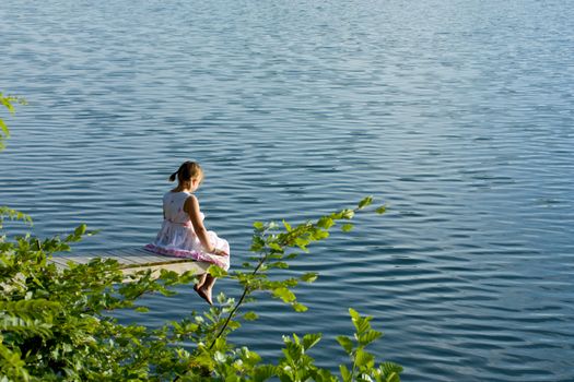 Girl in summer dress sitting at deck looking over water