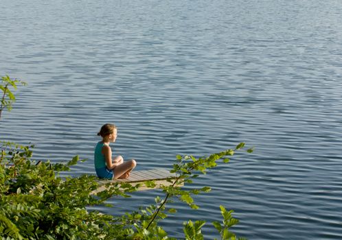 Little girl sitting crosslegged by a lake meditating