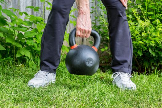 fitness workout with a heavy iron competition kettlebell (62lb/28 kg) on green grass in backyard - outdoor fitness concept