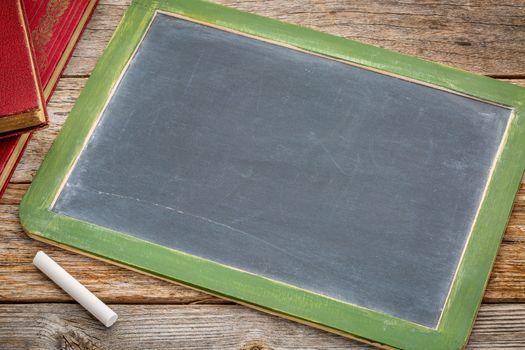 blank slate blackboard with a white chalk and a stack of books against rustic wooden table