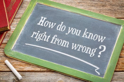 How do you know right from good - ethics question on a slate blackboard with a white chalk and a stack of books against rustic wooden table