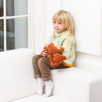 smiling little girl with teddy bear sitting on sofa at home