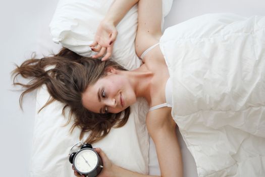 young woman in bed with alarm clock