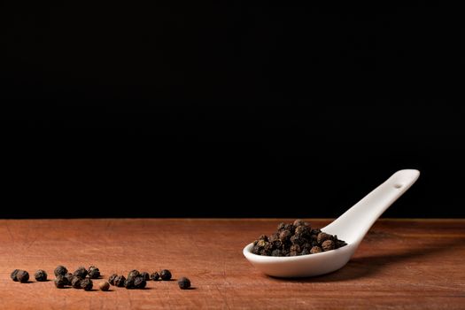 Peppercorns (piper nigrum) threads on a white porcelain spoon