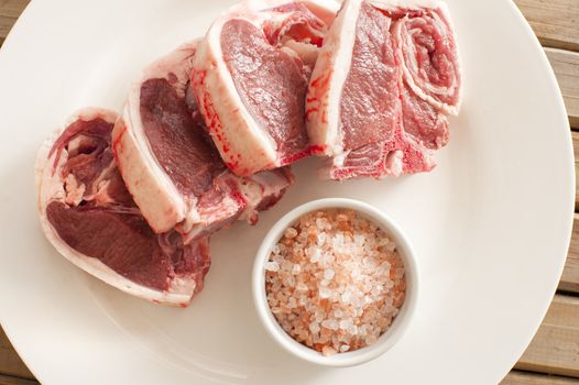 Top View of Fresh Lamb Meat Chops on White Round Plate with Rock Salt on a Saucer.