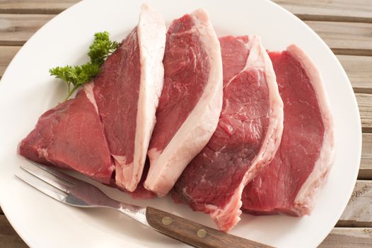 Close up Fresh Beef Steak on a White Round Plate with Fork, Placed on Top of a Wooden Table.