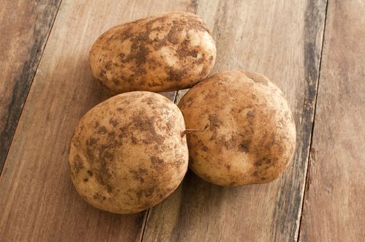 Close up Three Unwashed Fresh Potatoes on Top of a Wooden Table.