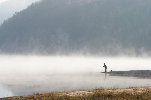 Man fishing at river shore in the morning.