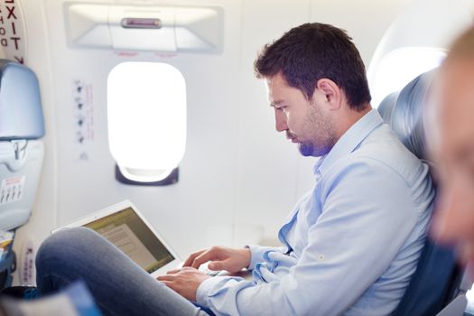 Casually dressed middle aged man working on laptop in aircraft cabin during his business travel. Shallow depth of field photo with focus on businessman eye.