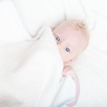 Cute blonde little baby boy with blue eyes hiding under the blanket.