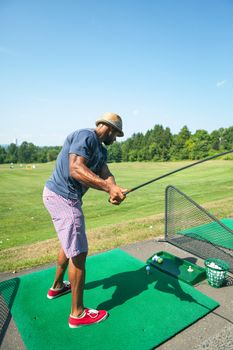 Athletic golfer swinging at the driving range dressed in casual attire.