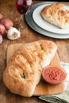 Homemade stromboli or stuffed bread with broccoli potatoes garlic onions and mozzarella cheese along with a side of marinara dipping sauce.