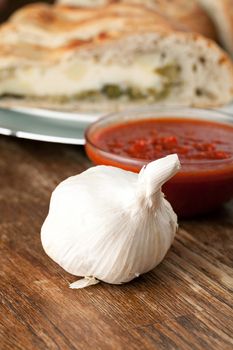 Garlic bulb closeup with tomato sauce in the background.  Shallow depth of field.