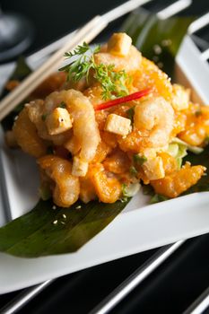 Thai crispy shrimp dish with apple and sesame seeds presented beautifully on a white square plate with chopsticks.