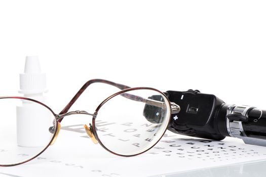 Glasses, ophthalmoscope and a bottle of eye drops are on a vision test