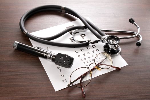 Glasses, ophthalmoscope and a stethoscope are on a vision test