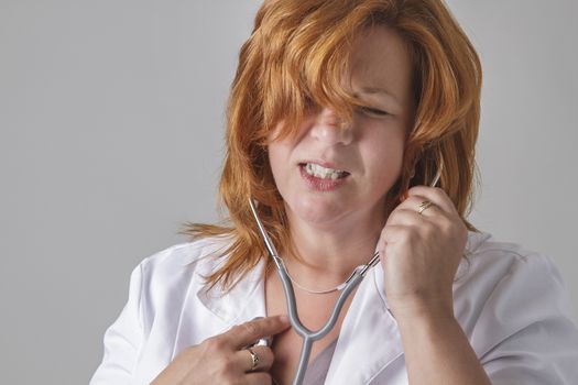 forty something woman with red hair, listening to her heart with a stethoscope with pain expression