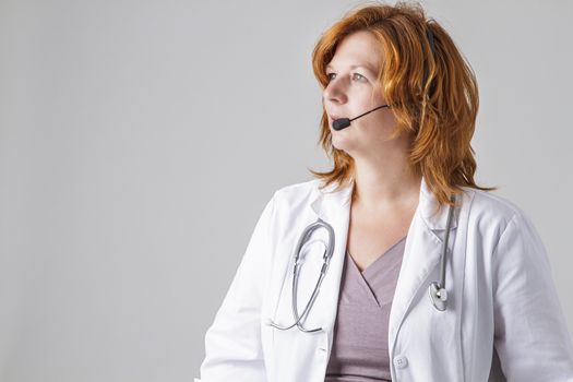 woman in her forties wearing a white lab coat and a headset looking toward the left