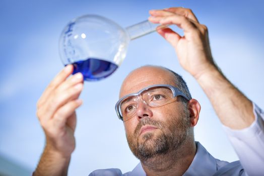 Chemist with safety goggles examining a blue liquid