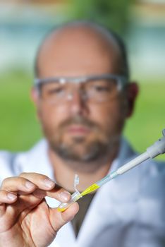 Chemist with safety goggles examining a yellow liquid