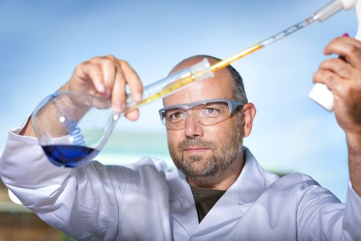 Chemist with safety goggles examining a blue liquid