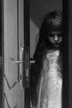 A creepy little girl staring from behind the door