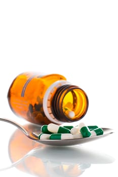 Tablets on a spoon with a brown bottle, on a white background