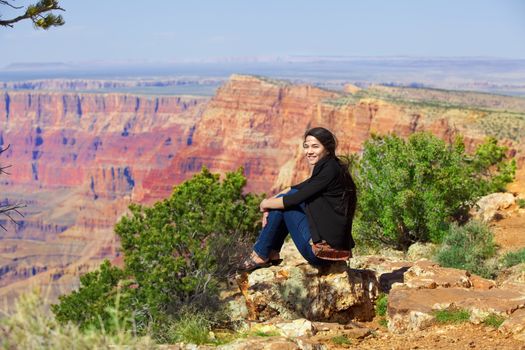 Biracial teen girl sitting along rock ledge at Grand Canyon, Arizona