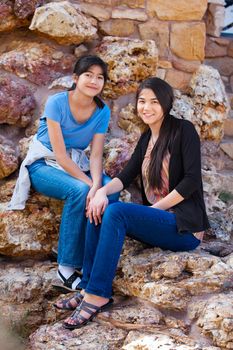 Two biracial  young teen girls, sisters or friends,  sitting together on rocky stone seats outdoors