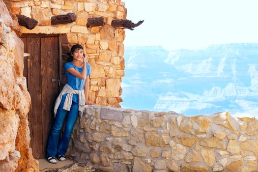 Biracial teen girl relaxing, leaning against rock wall overlooking Grand Canyon, next to doorway